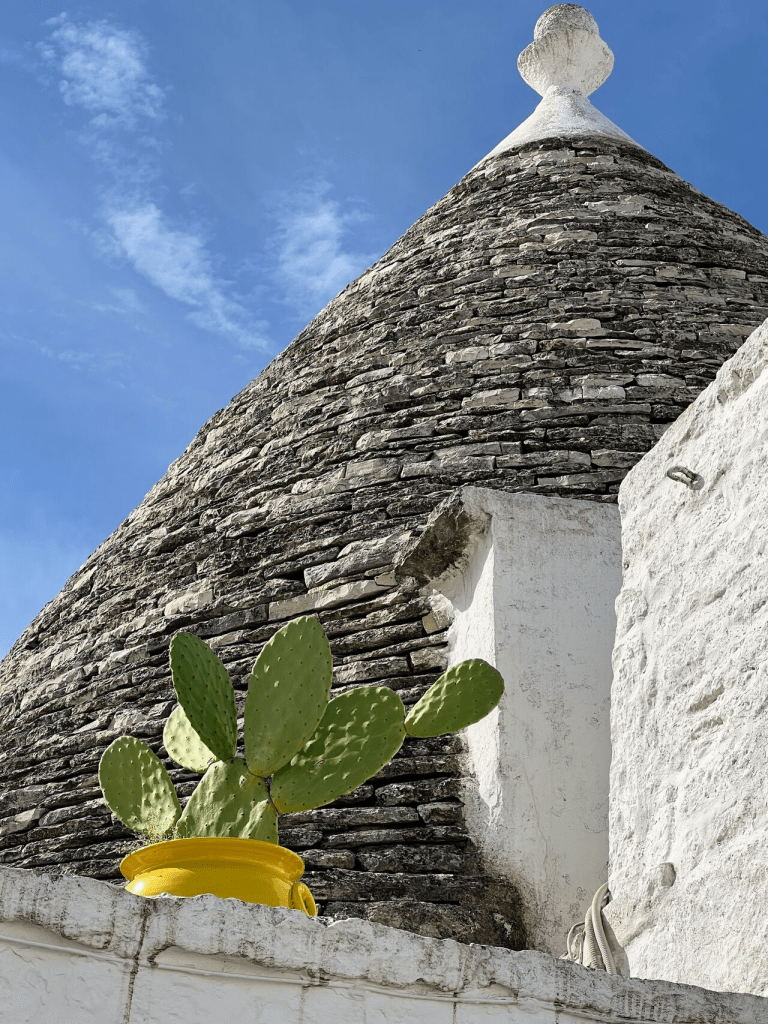Trullo in Puglia met blauwe lucht en groene cactus in gele pot. Heldere kleuren die eenvoud symboliseren. 